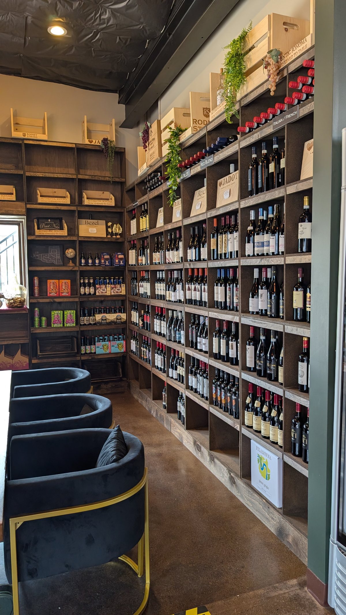 The Open BTL retail wall: floor-to-ceiling wine shelves beside velvet chairs