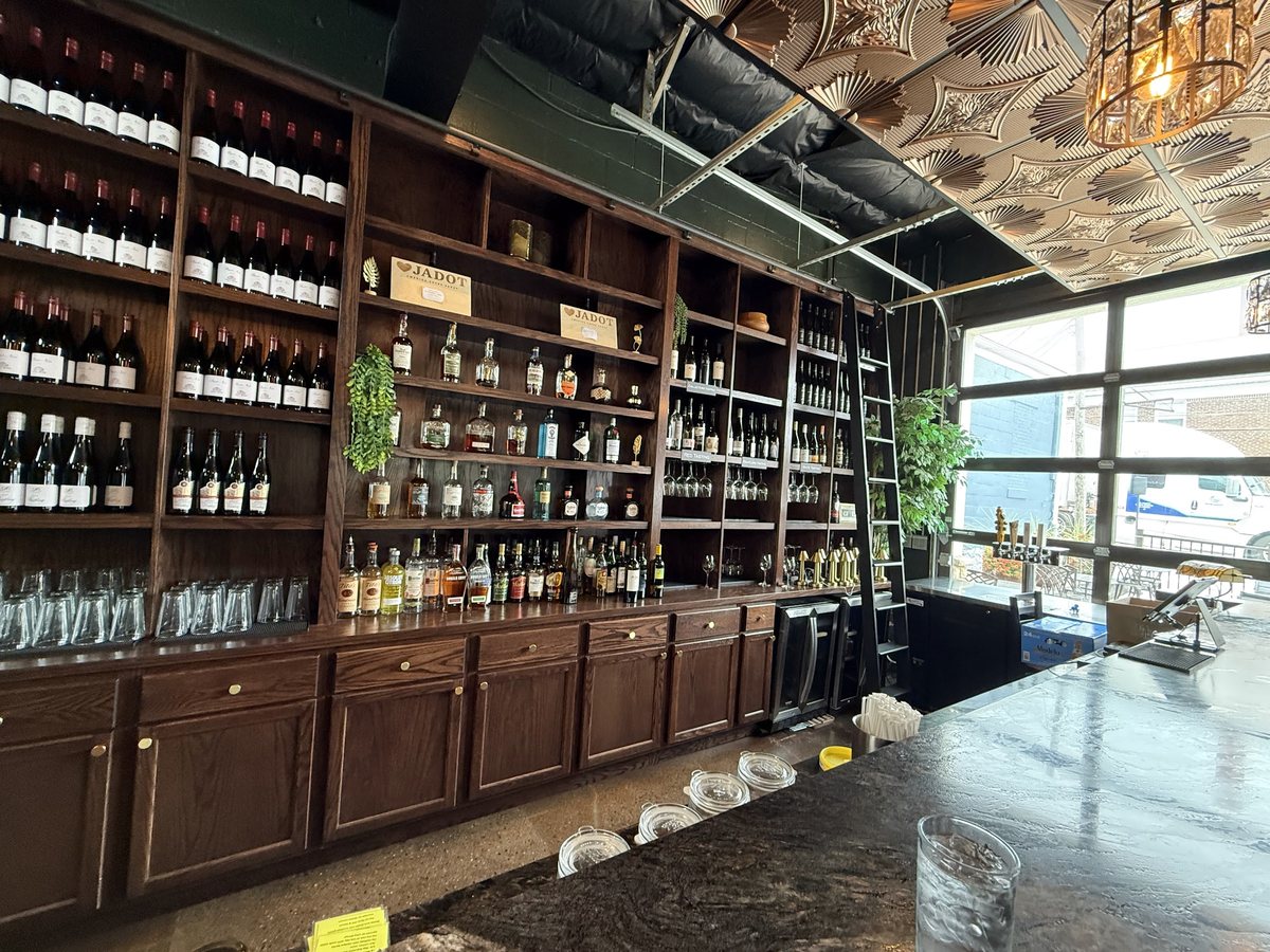 The Open BTL bar: dark wood cabinets and a floor-to-ceiling wall of bottles under a pressed-tin ceiling